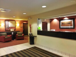 A hotel reception area with a reception desk, a 'WELCOME' sign, a clock, and a seating area with chairs and a lamp.