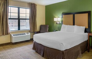 A hotel room with a large bed, a chair, a desk, a lamp, and a window with curtains. - Extended Stay America Suites Columbus NE I270 (Columbus)