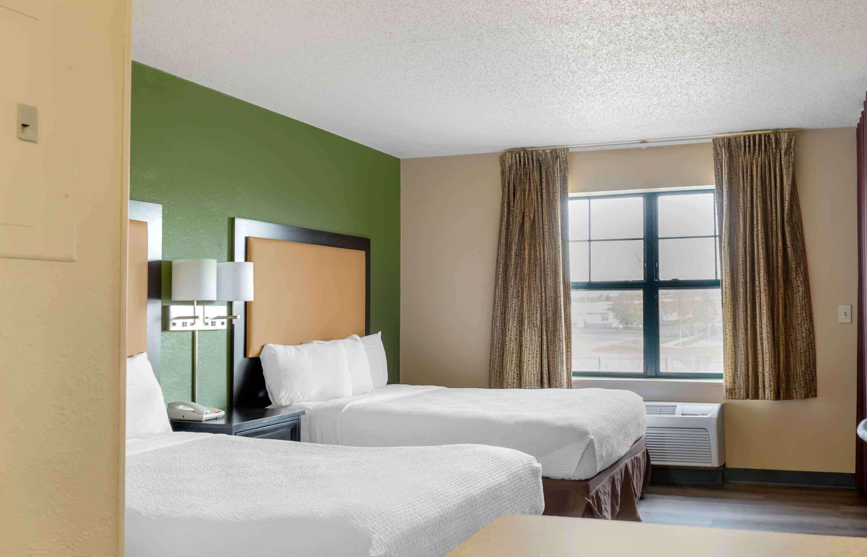 Habitación de hotel con dos camas, un escritorio con lámpara, teléfono y ventana con cortinas.