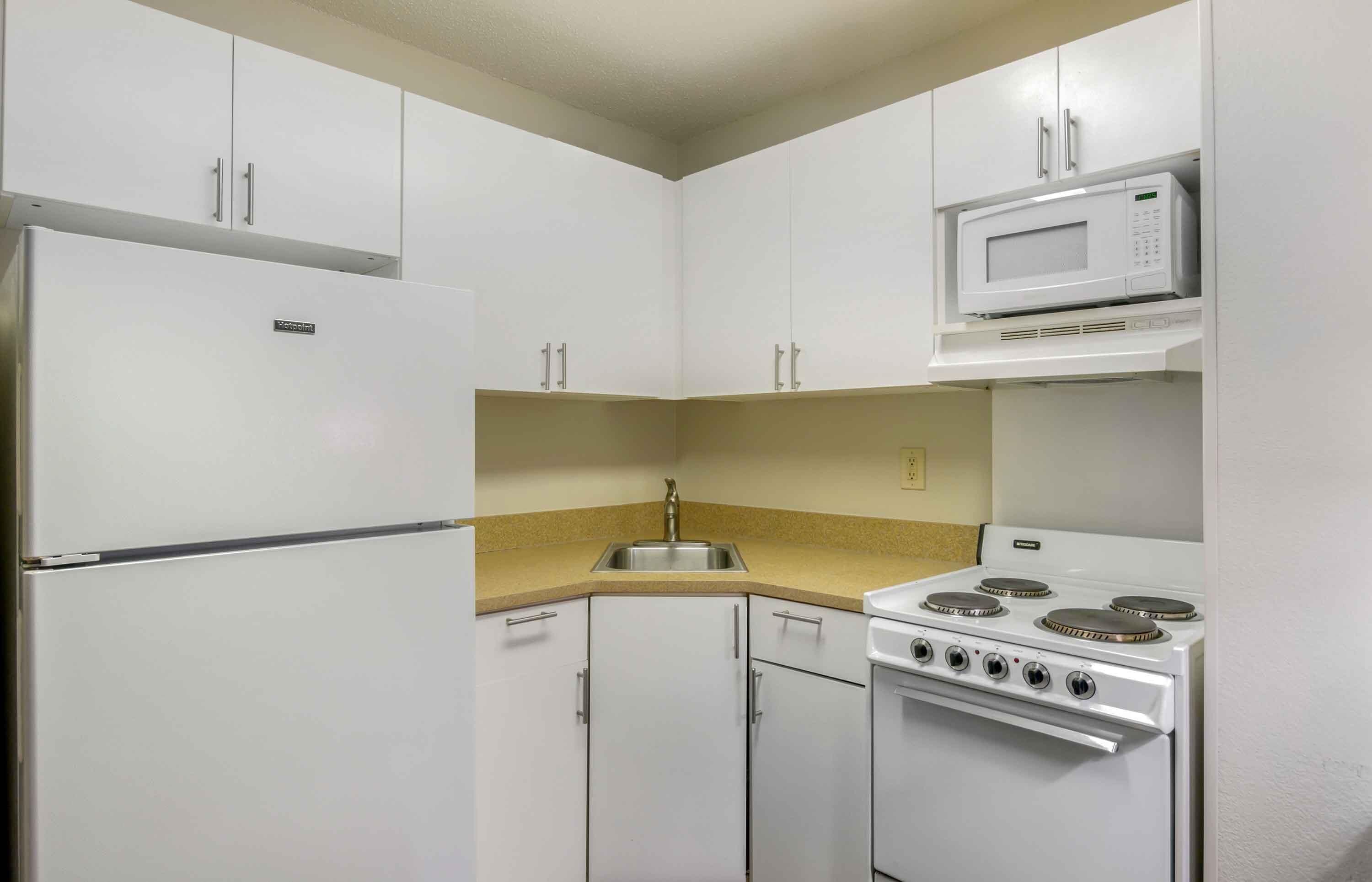 A compact kitchen with white cabinets, a stainless steel sink, a microwave, and a stove.