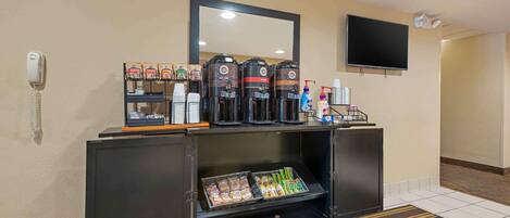Zona de recepción de un hotel con estación de café, teléfono, televisor y espejo.