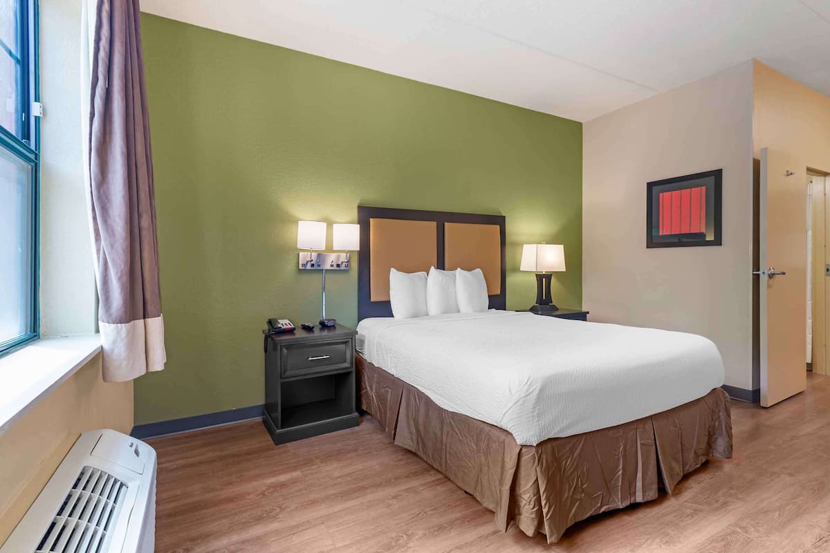 Une chambre d’hôtel avec un grand lit, des lampes de chevet, une table de nuit, une fenêtre avec des rideaux et une porte.