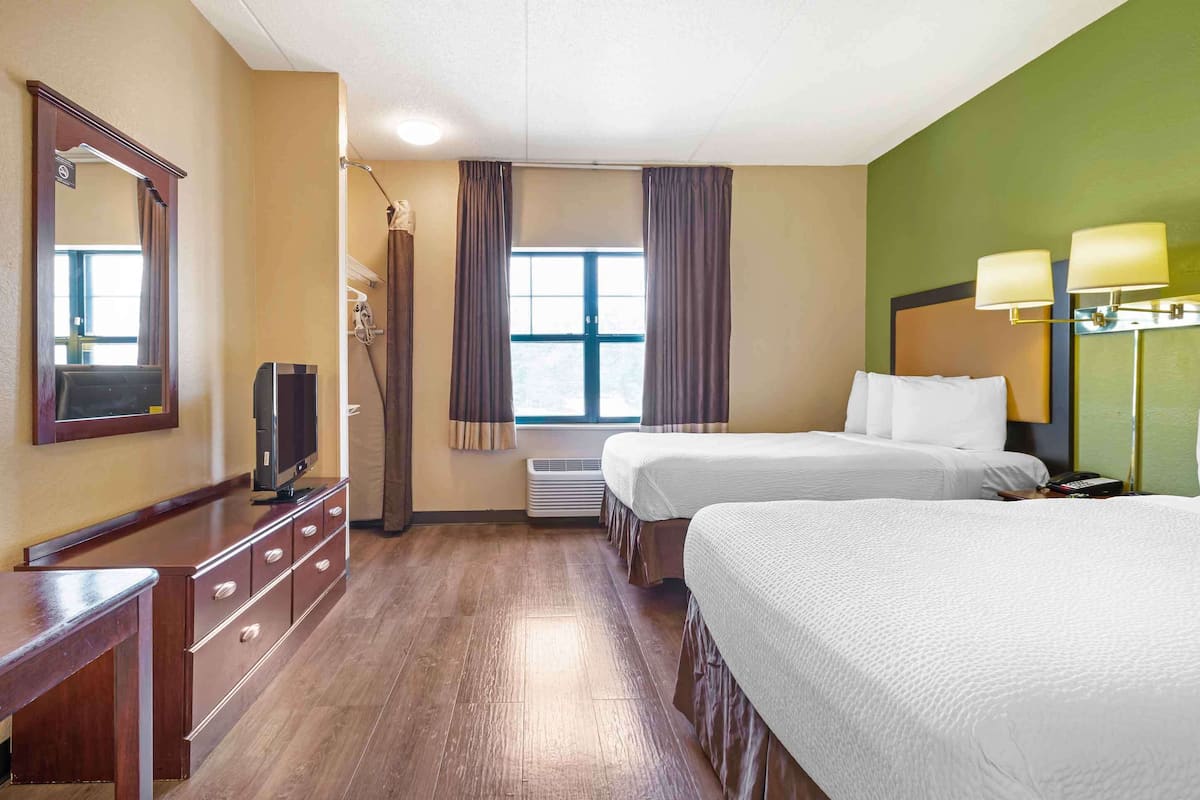 Une chambre d’hôtel avec deux lits, une télévision, une commode et une fenêtre avec des rideaux.