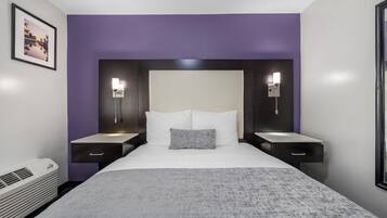A modern hotel room with a large bed, two bedside tables, a nightstand, a wall-mounted lamp, and a framed picture on the wall.