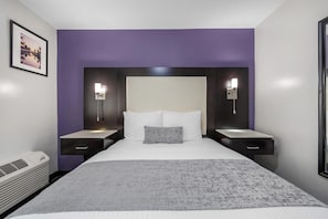 A modern hotel room with a large bed, two bedside tables, a nightstand, a wall-mounted lamp, and a framed picture on the wall.