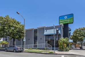 A modern hotel with a blue awning, a street sign, and a parked car.