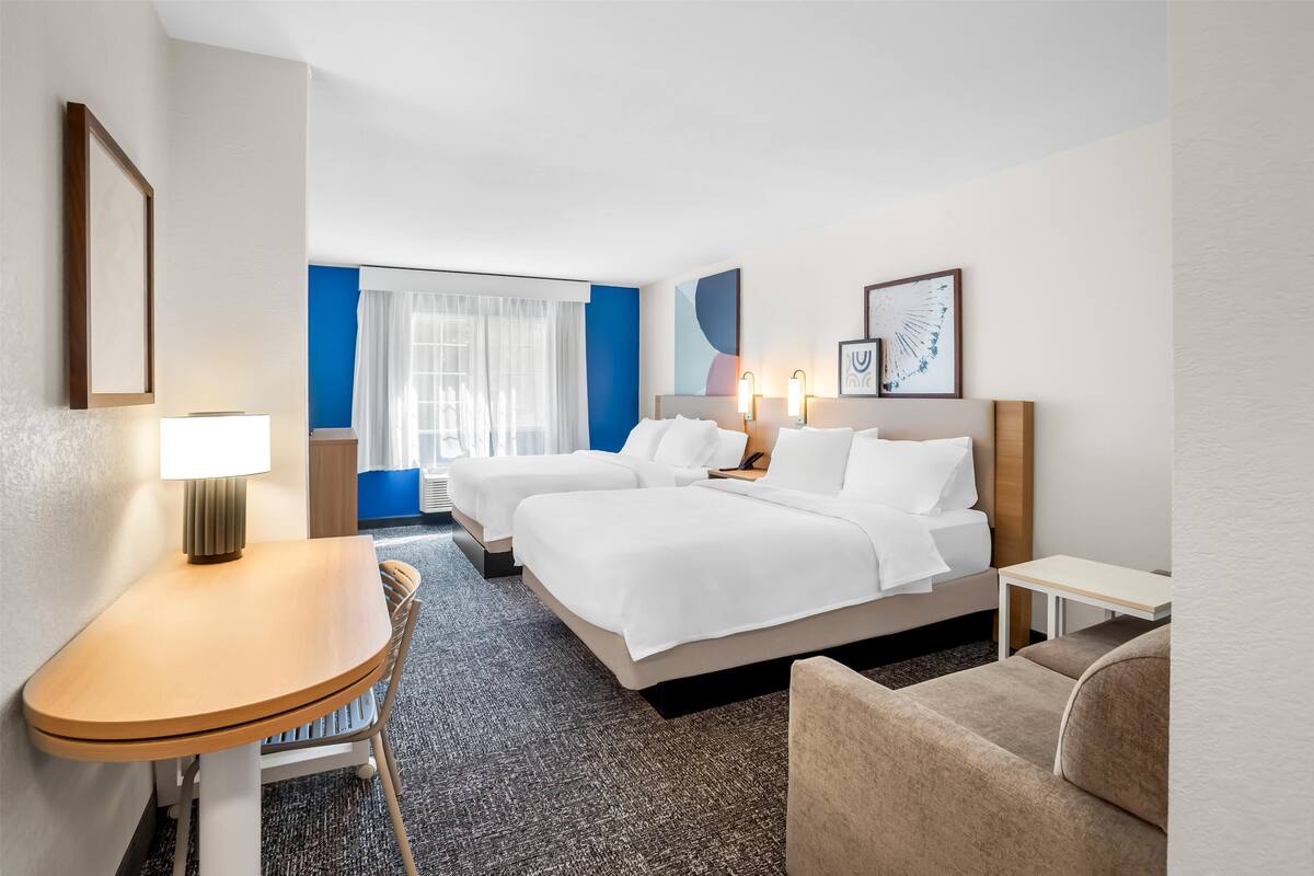 Una habitación de hotel con dos camas, un escritorio, una silla y una mesita.