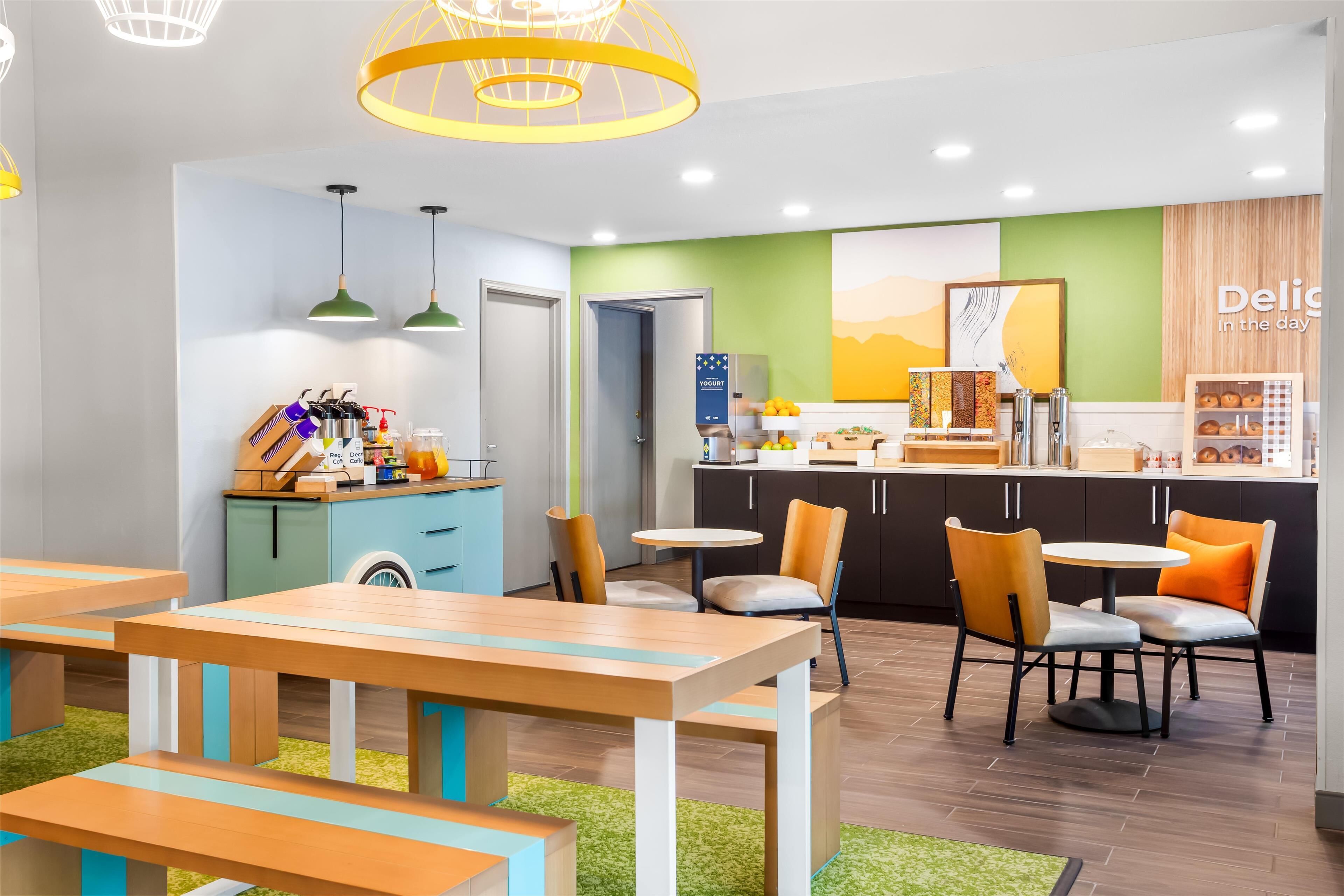 A modern cafe with wooden tables and chairs, a yogurt dispenser, and a counter with various food items.