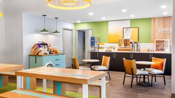 Un café moderno con mesas y sillas de madera, un dispensador de yogur y una barra con diversas opciones de comida.