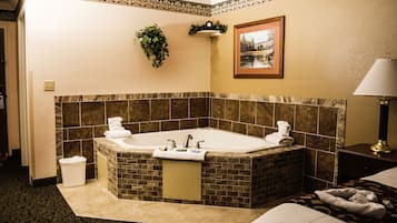 Une salle de bain avec une grande baignoire, un lavabo et un miroir. On y trouve un porte-serviettes avec des serviettes, une horloge et un tableau encadré au mur.