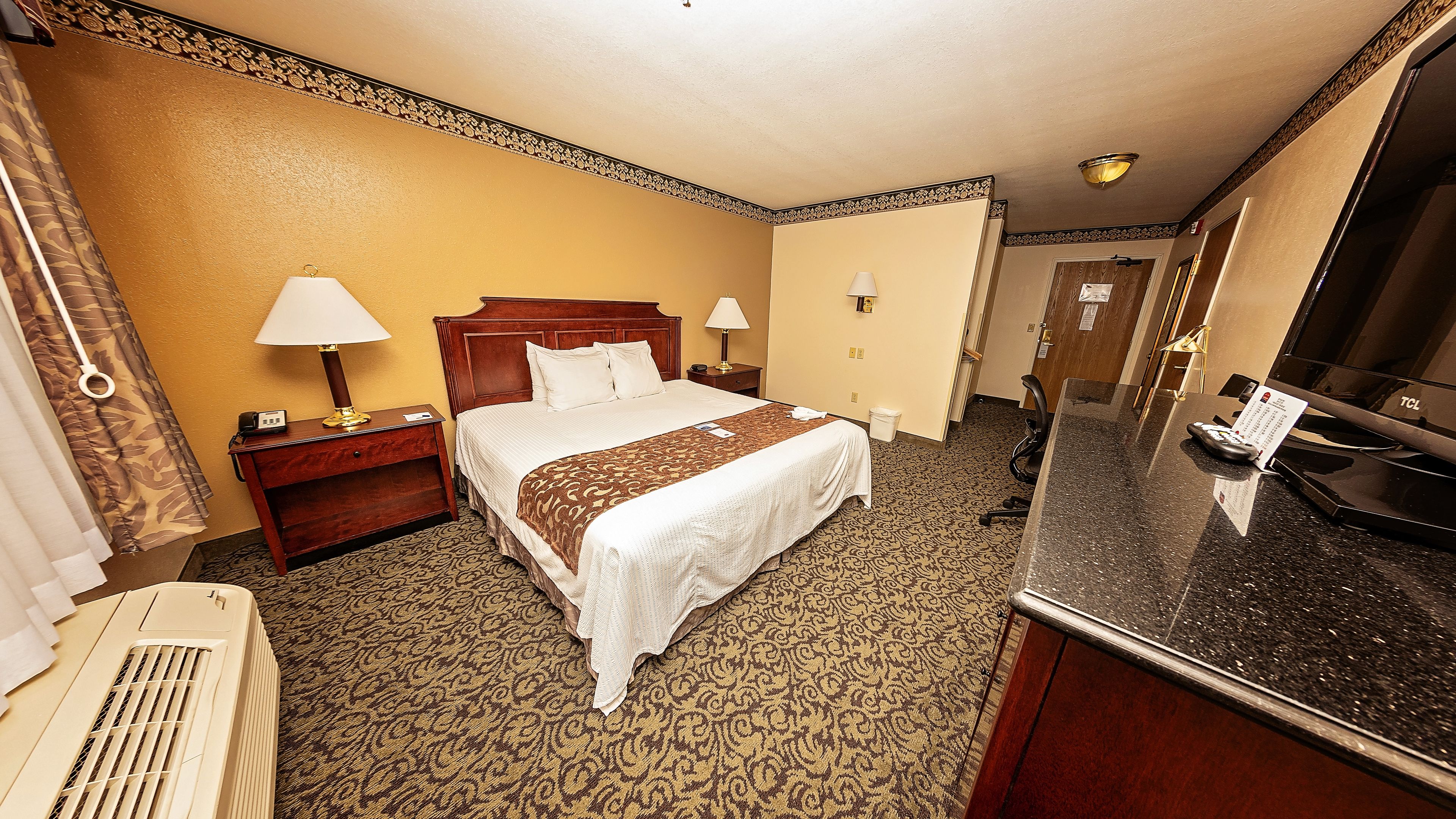 Habitación de hotel con una cama grande, dos mesitas de noche con lámparas, un escritorio con ordenador, televisión de pantalla plana y minibar.
