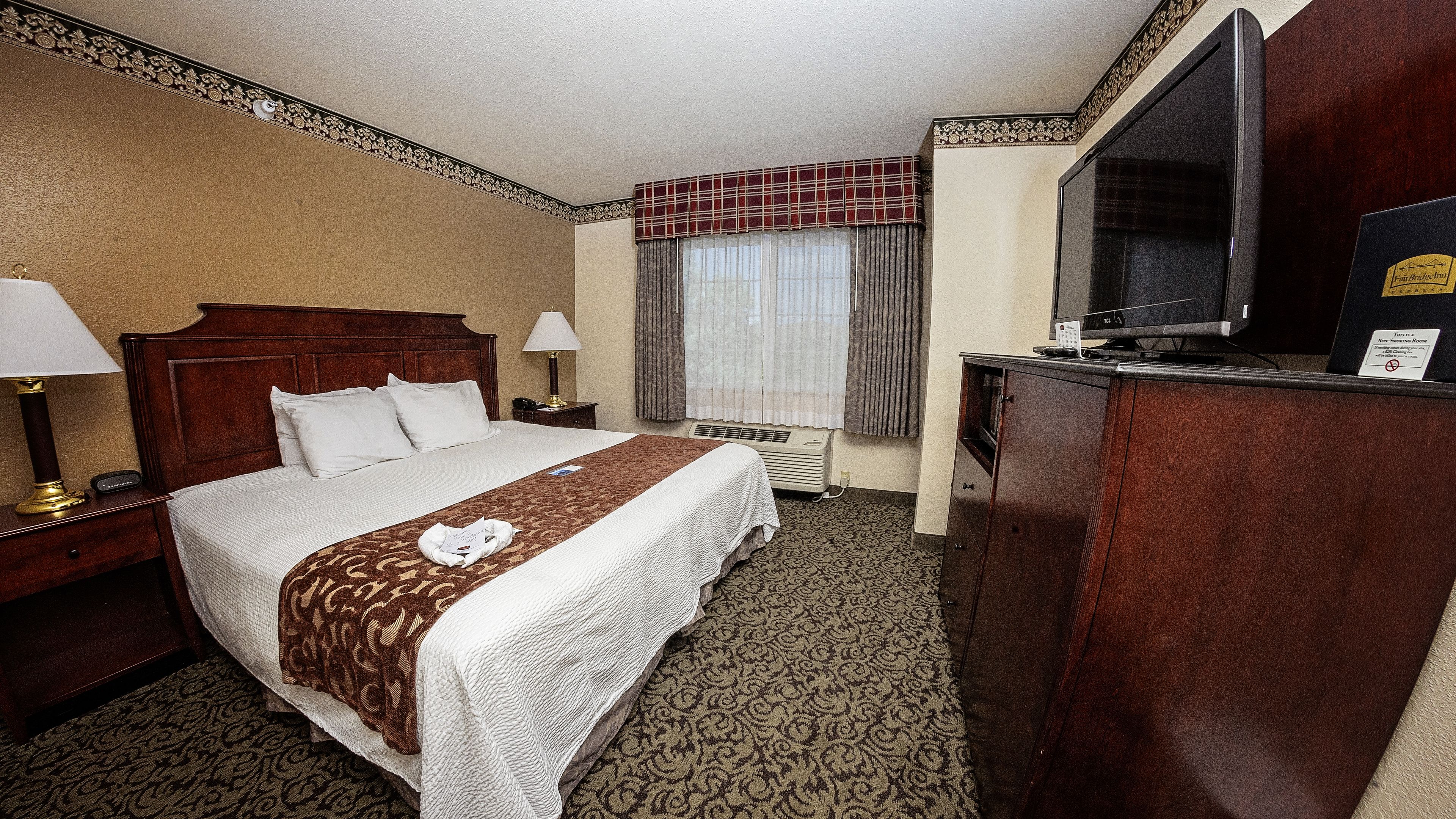 Een hotelkamer met een bed, een bureau, een televisie en een raam met gordijnen.