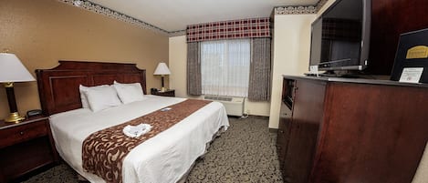 A hotel room with a bed, a desk, a television, and a window with curtains.