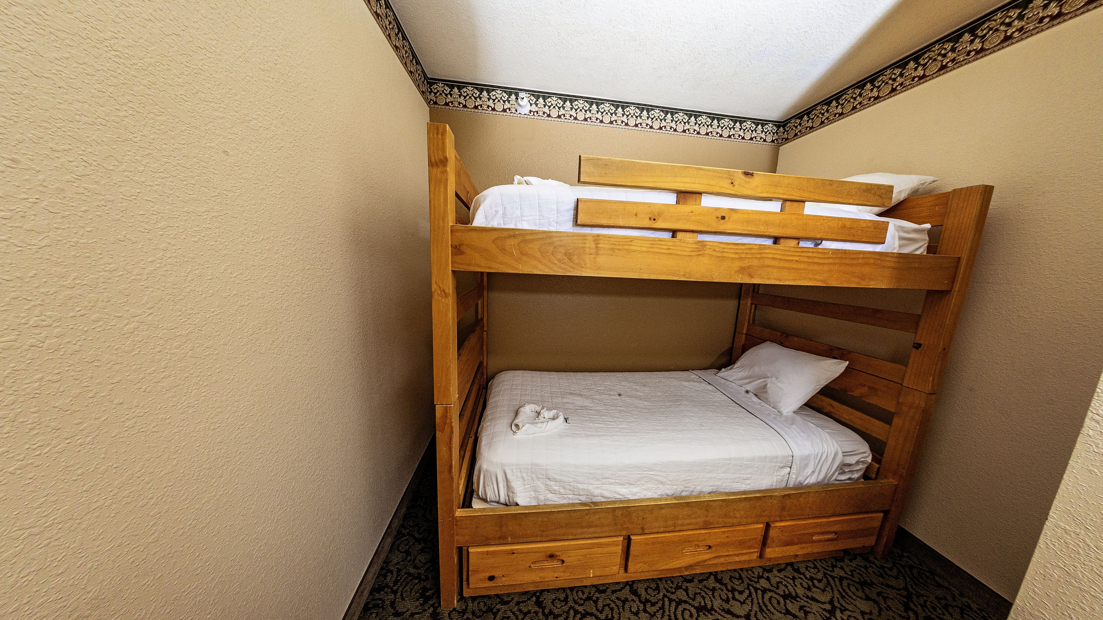 Ein Stockbett mit Holzrahmen, weißer Bettwäsche und einem gemusterten Teppich.