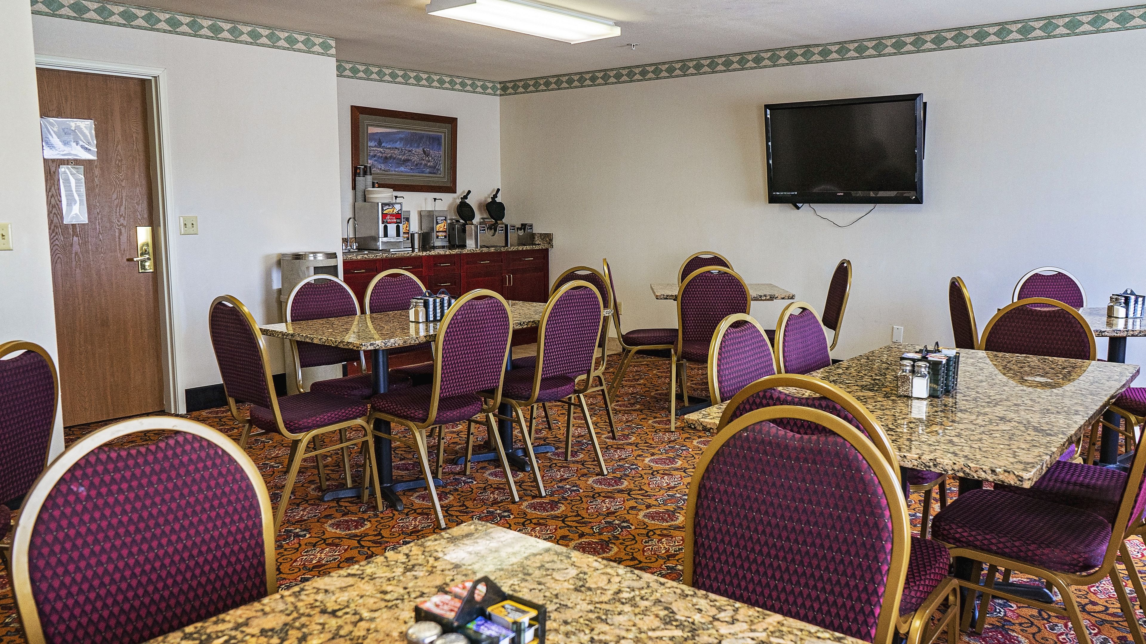 Un salón de conferencias con una larga mesa, varias sillas, un televisor y una estación de café.