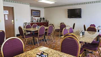 Un salón de conferencias con una larga mesa, varias sillas, un televisor y una estación de café.