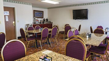 Un salón de conferencias con una larga mesa, varias sillas, un televisor y una estación de café.