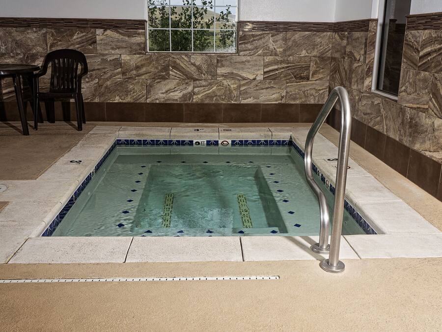 A rectangular indoor pool with a metal ladder, surrounded by stone walls and a tiled floor.