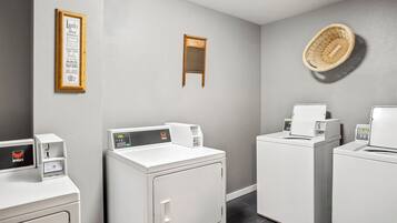 A laundry room with white washers and dryers, a framed laundry instruction sign, and a woven basket on the wall.