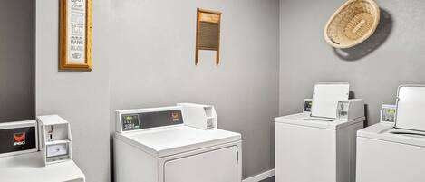 A laundry room with white washers and dryers, a framed laundry instruction sign, and a woven basket on the wall.