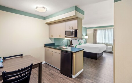 A compact hotel room with a kitchenette, a bed, and a dining area.