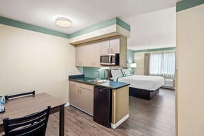 A compact hotel room with a kitchenette, a bed, and a dining area.