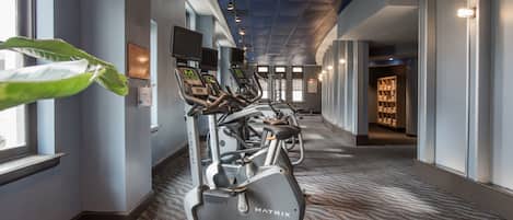 A fitness center with treadmills and exercise equipment, carpeted floors, and large windows.