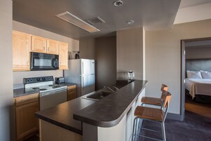 Una cocina moderna con armarios de madera, un microondas negro, un refrigerador blanco y una estufa. Hay una zona de bar con dos taburetes y un lavamanos.