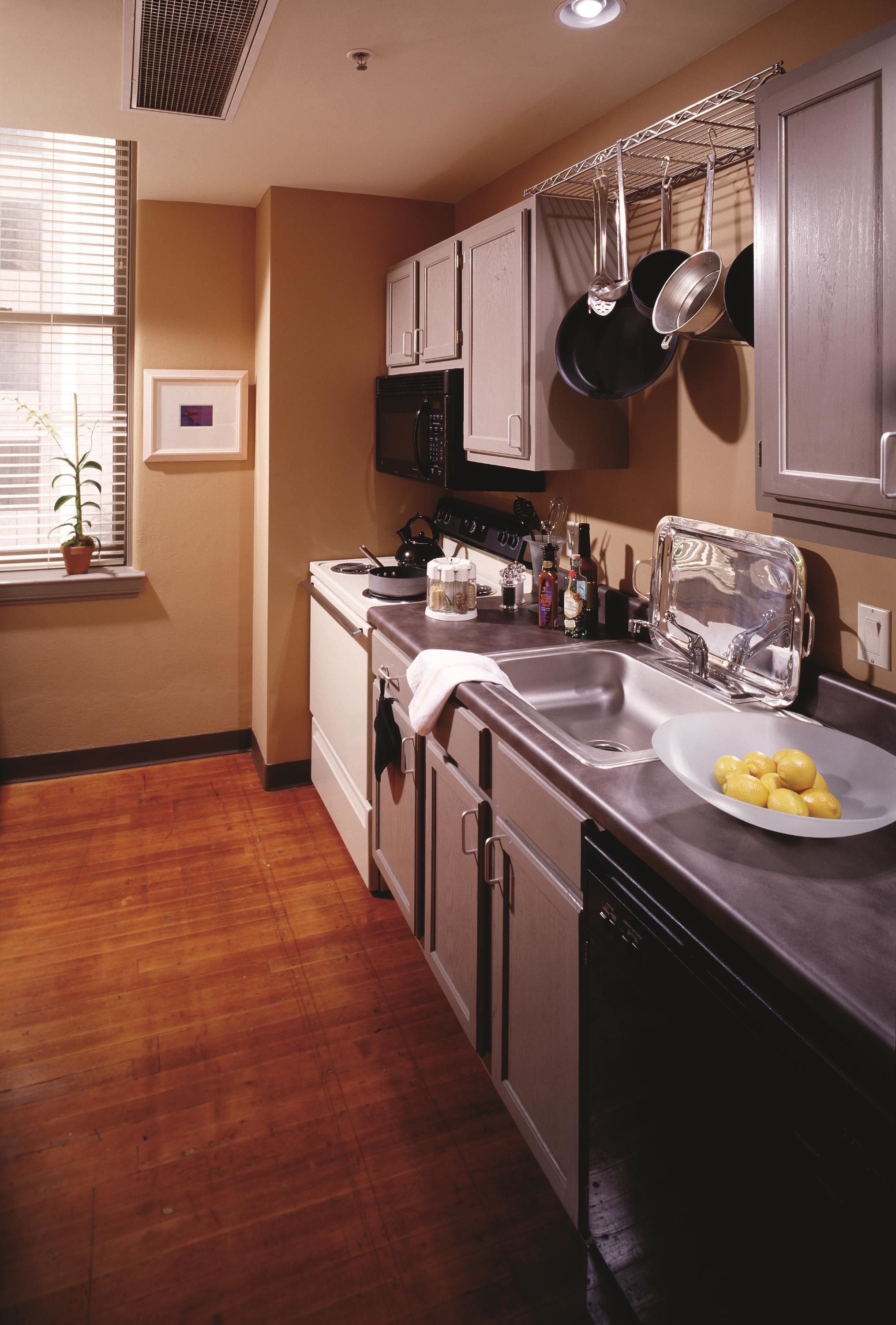 A kitchen with wooden flooring, stainless steel appliances, and a window with blinds.