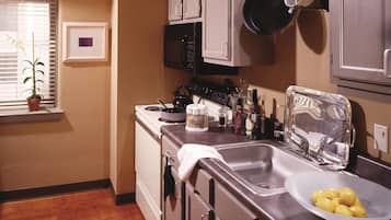 A kitchen with wooden flooring, stainless steel appliances, and a window with blinds.