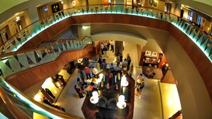 A spacious atrium with a central seating area, multiple levels with glass railings, and a variety of lighting fixtures. - Magnolia Hotel Dallas Downtown (Dallas)