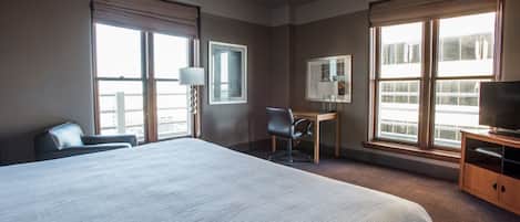 Une chambre d’hôtel avec un grand lit, un bureau, une chaise, une télévision et de grandes fenêtres.