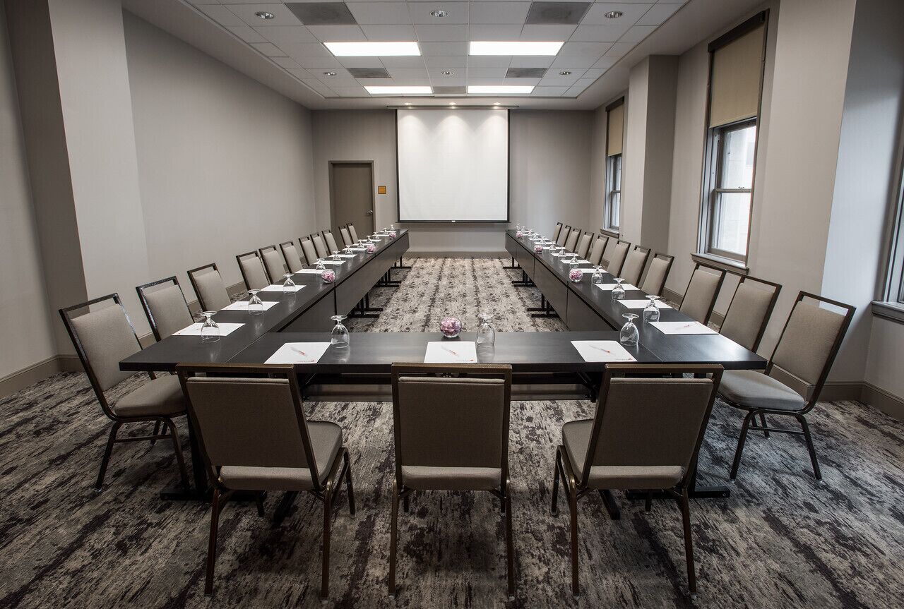 Une salle de conférence avec une longue table, des chaises, un écran de projection et un sol recouvert de moquette.