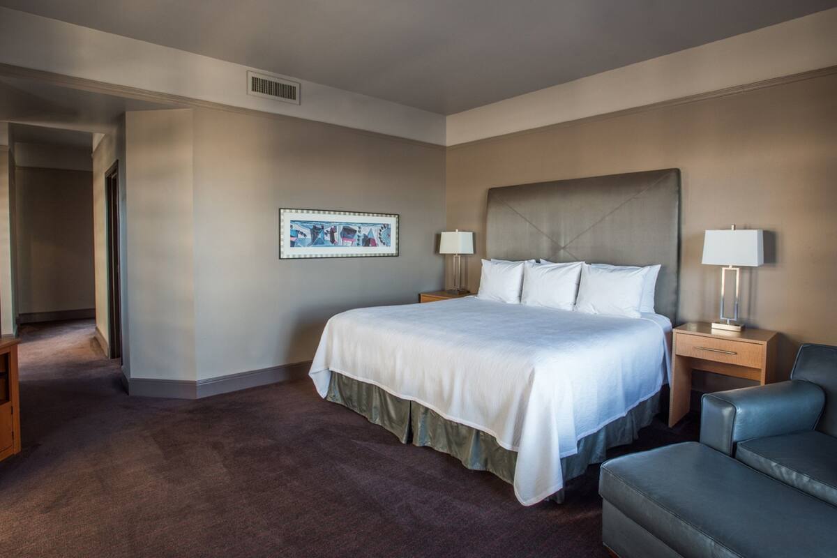 A hotel room with a large bed, two bedside tables with lamps, a desk, a chair, and a framed picture on the wall.