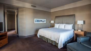 Habitación de hotel con una cama grande, dos mesitas de noche con lámparas, un escritorio, una silla y un cuadro enmarcado en la pared.
