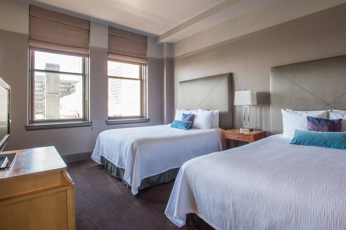 A hotel room with two beds, a desk, and a window with blinds.