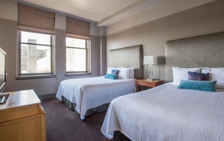Een hotelkamer met twee bedden, een bureau en een raam met zonwering.