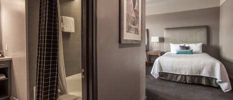 A hotel room with a shower, a bed with a headboard, a nightstand, and a framed picture on the wall.