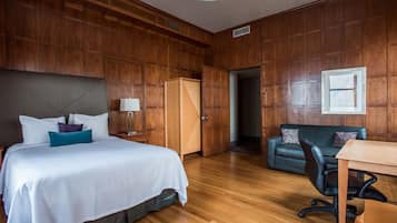 A hotel room with a wooden paneled wall, a bed with white bedding, a desk with a chair, and a green sofa.