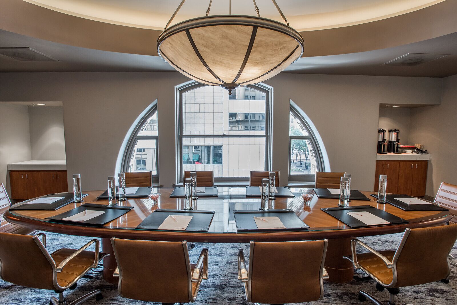 A conference room with a large oval table, leather chairs, and a central chandelier.