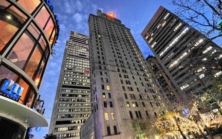 A high-rise building with multiple floors and numerous windows, surrounded by other tall buildings.