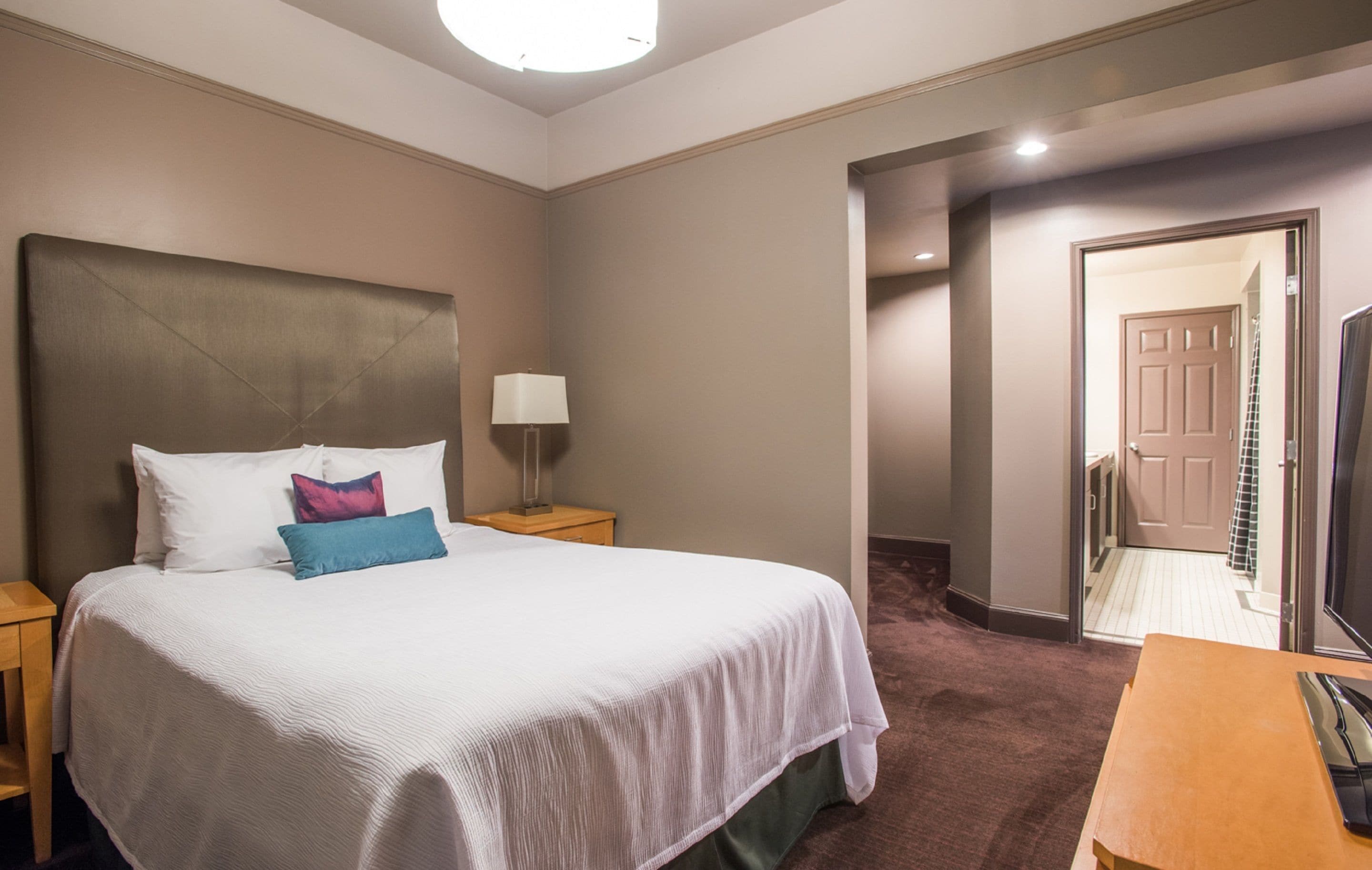 Une chambre d’hôtel avec un grand lit, une table de chevet avec une lampe, une commode en bois et un bureau avec un téléphone.