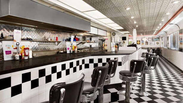 A restaurant with a checkered floor, bar stools, and a counter with various condiments and a menu. - Baymont by Wyndham Hearne (Hearne)