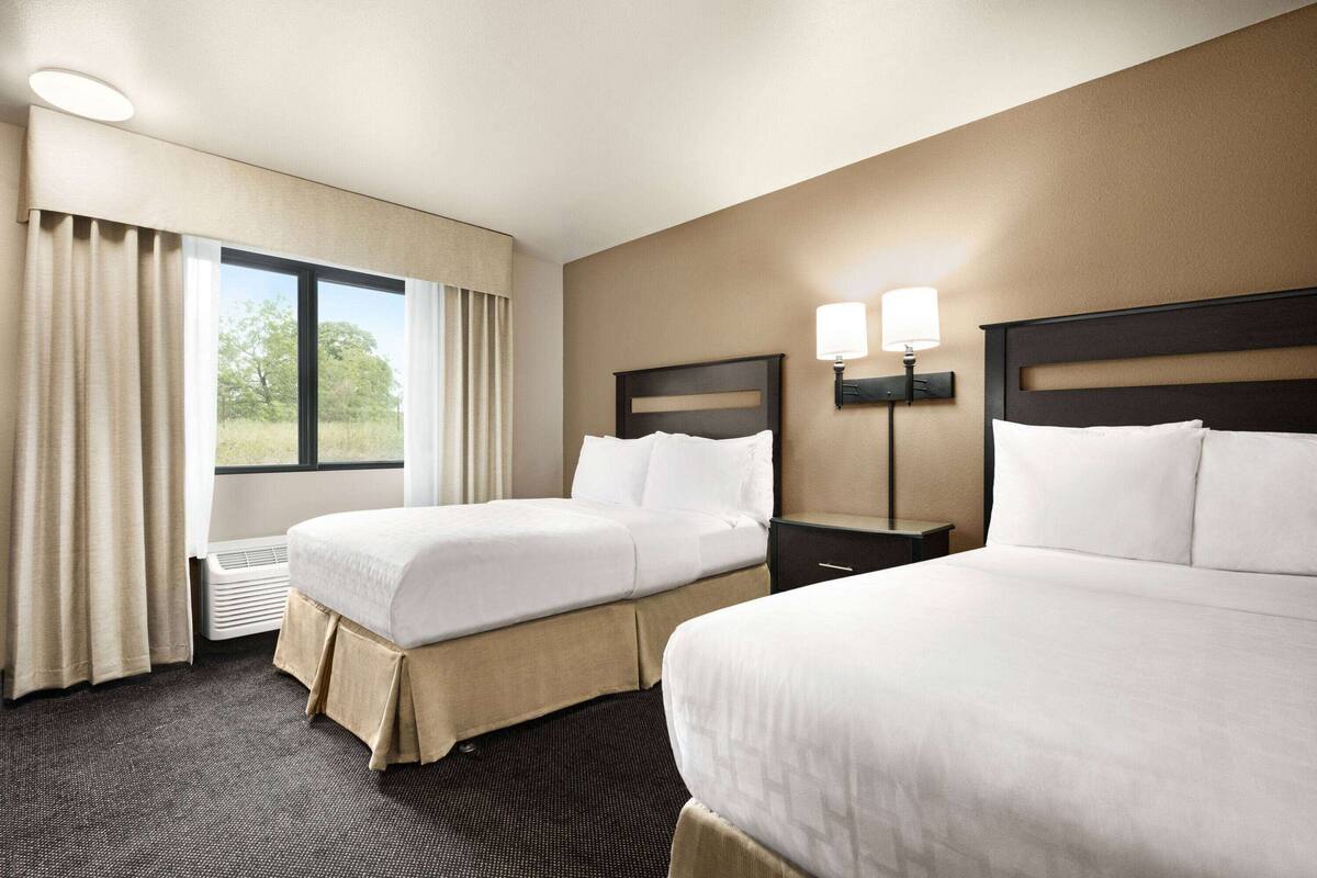 Habitación de hotel con dos camas, una ventana con cortinas, una lámpara de pared y un radiador.