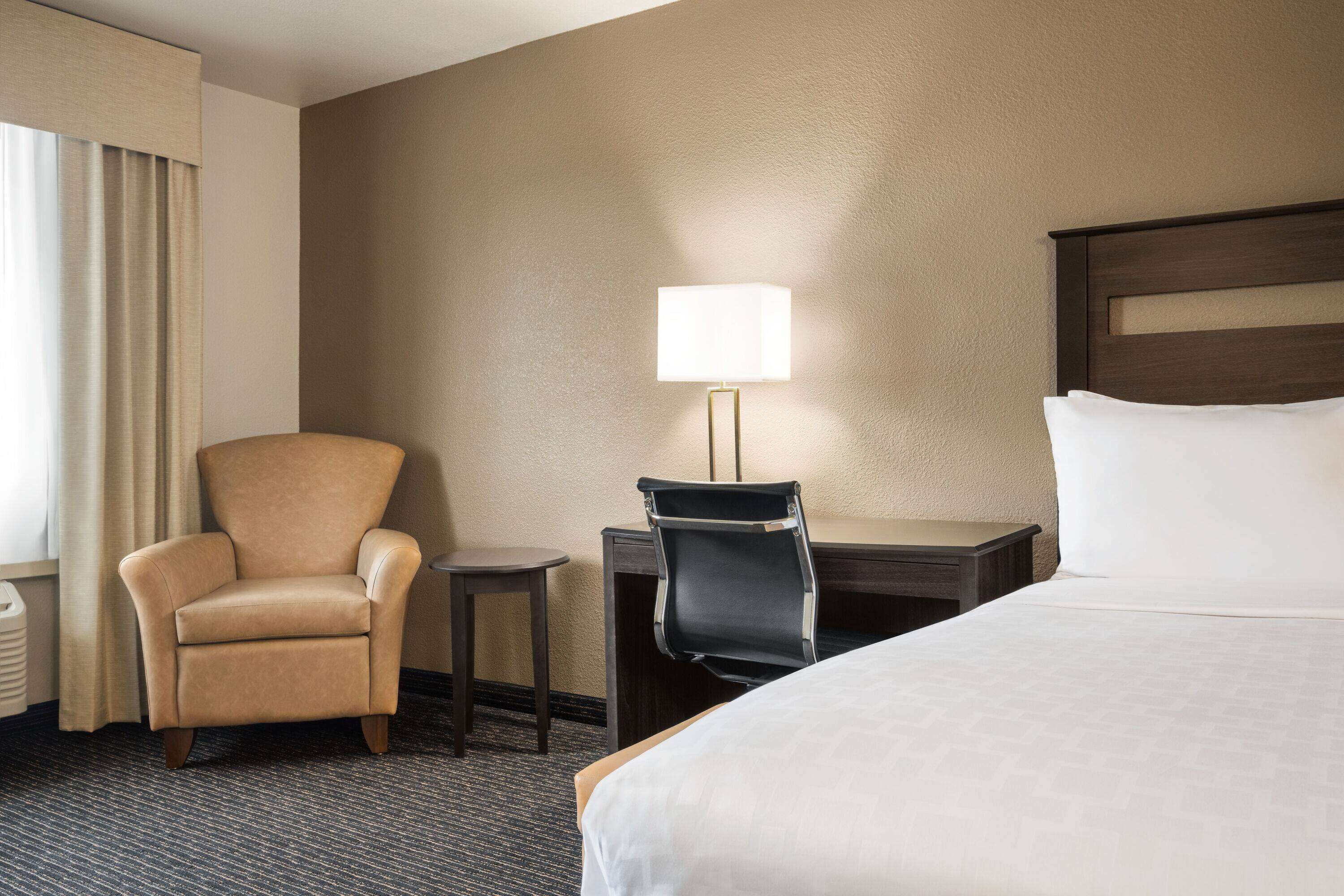 Una habitación de hotel con cama, una silla, un escritorio y una lámpara.