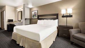 A hotel room with a large bed, a desk with a lamp, a chair, and a small cabinet. - Baymont by Wyndham Hearne (Hearne)