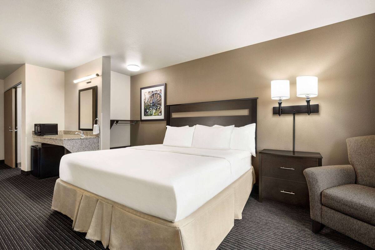Habitación de hotel con una cama grande, un escritorio con lámpara, una silla y un pequeño armario.
