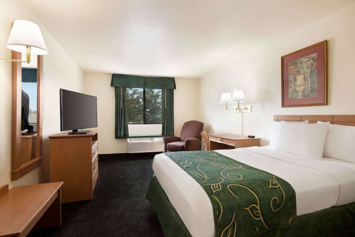 Una habitación de hotel con cama, escritorio, silla, televisor y ventana con cortinas.