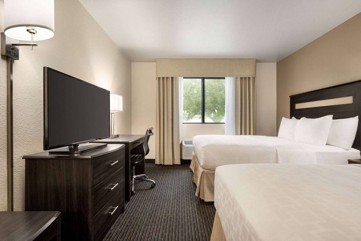 Habitación de hotel con televisión de pantalla plana, escritorio, dos camas, ventana con cortinas y lámpara de techo.