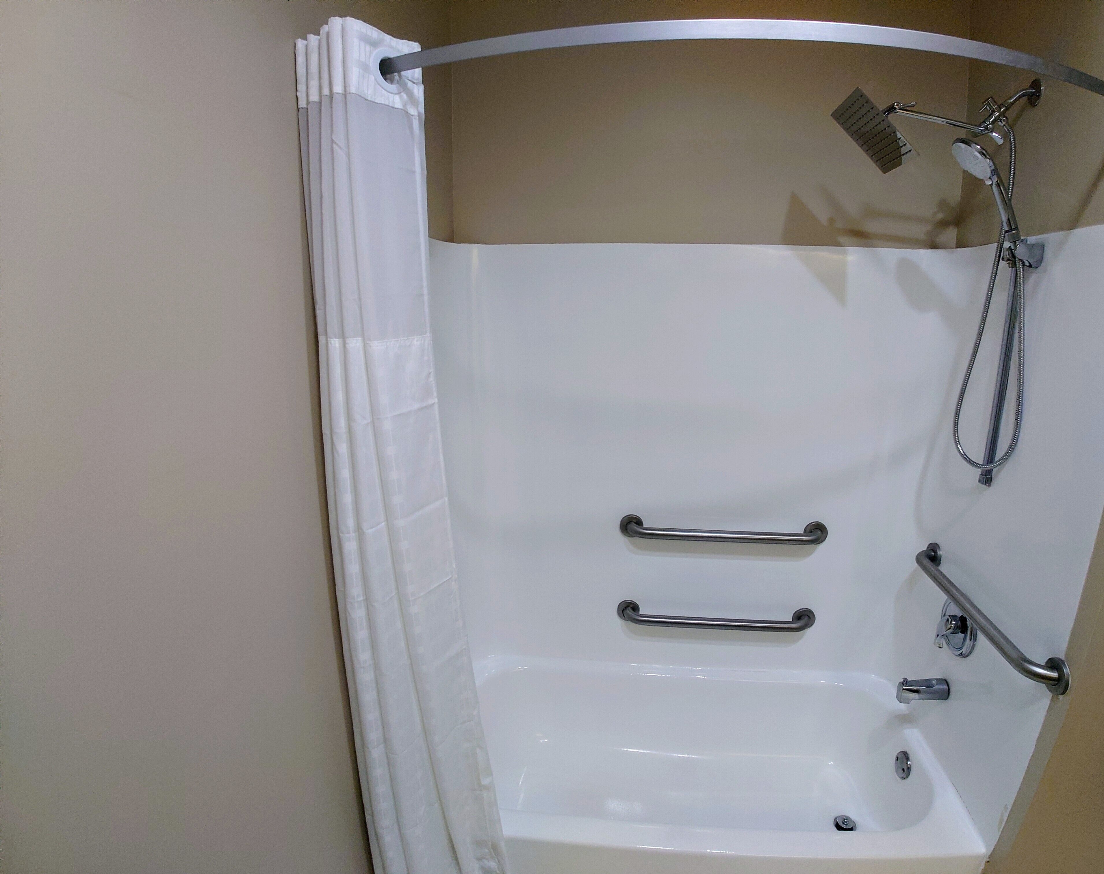 Une salle de bain équipée d’une baignoire, de barres d’appui, d’un pommeau de douche et d’un rideau de douche.